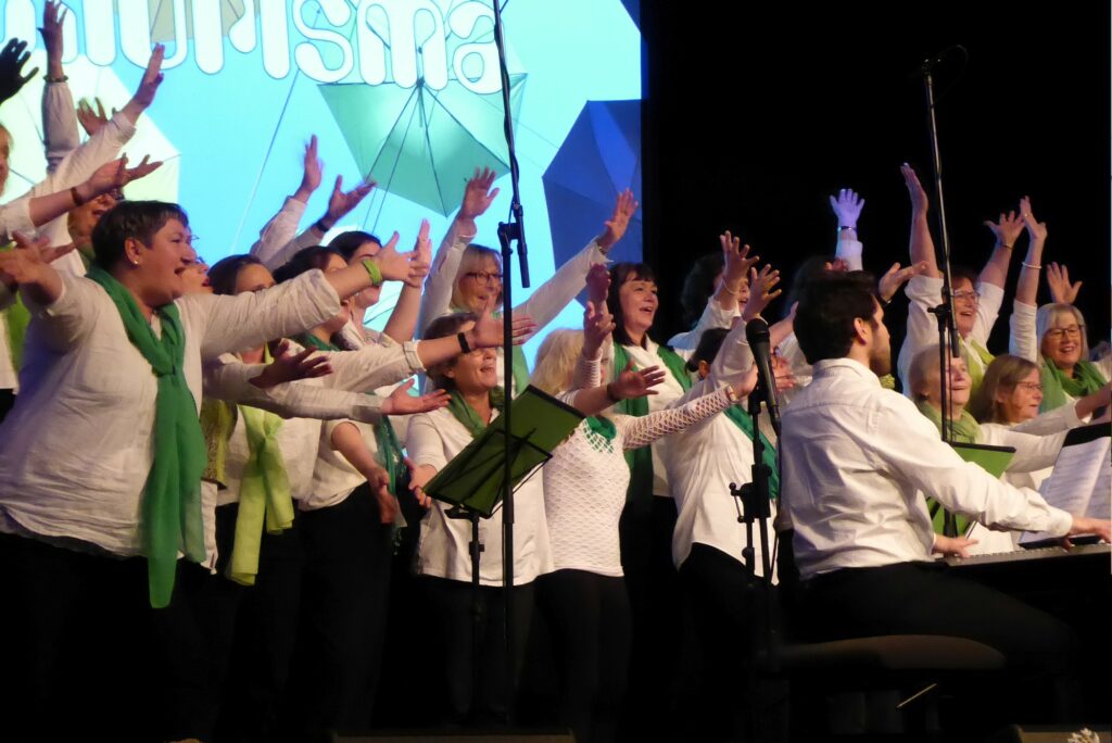 Die Chorisma-Sängerinnen heben beim Abschluss des Liedes gemeinsam die Arme in die Höhe.