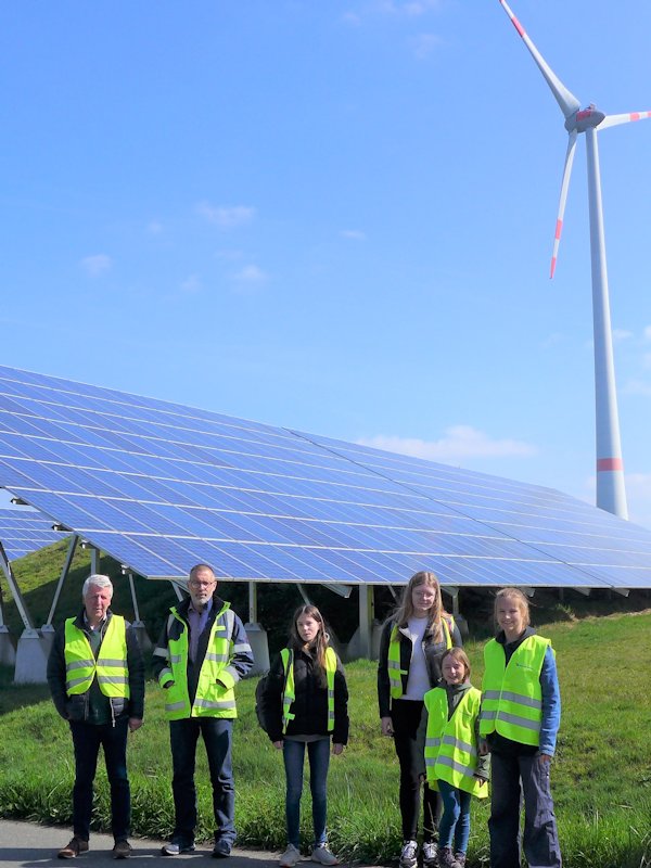 Vier Teilnehmerinnen und zwei Betreuer stehen vor einer Photovoltaikanlage. Im Hintergrund ist ein Windrad zu sehen.