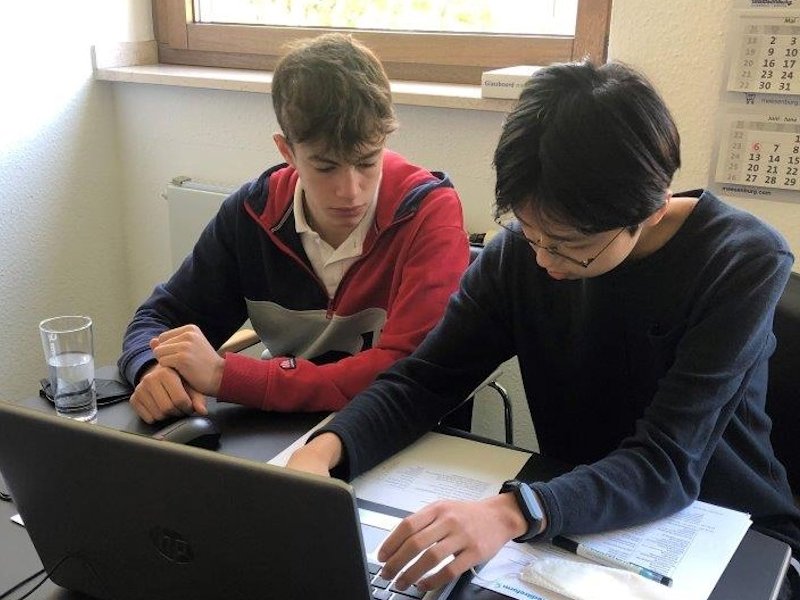 Zwei SDchüler sitzen vor einem Laptop und bearbeiten ihre Aufgaben.