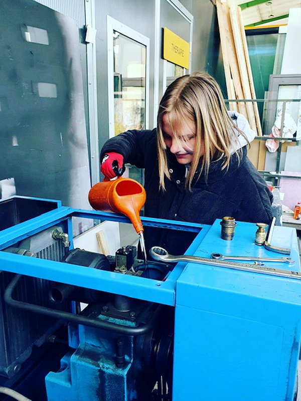 Eine Mädchen gießt eine Flüssigkeit in den Tank einer Maschine.