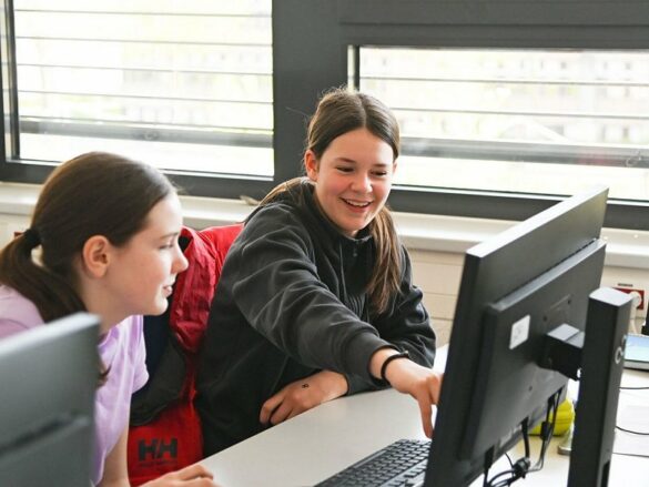 Zwei Mädchen sitzen lachend vor einem PC-Bildschirm.