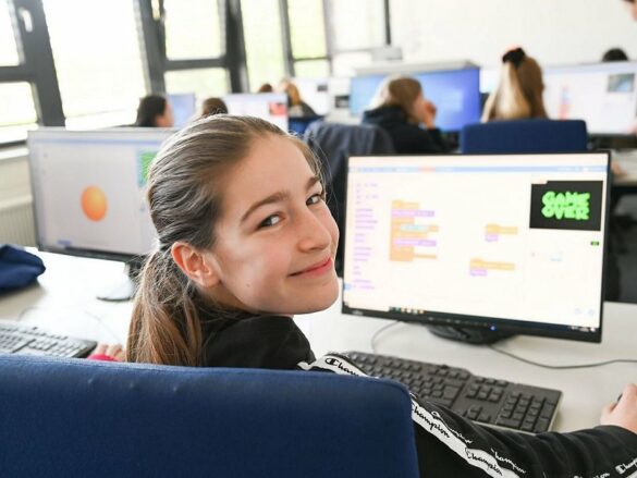 Ein Mädchen blickt lächenld über die Schluter und erfreut sich am Programmierergebnis.