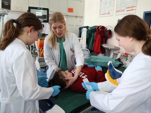 Eine Ärztin zeigt 2 Mädchen die korrekte Lagerung einer Patientin im Notfall.