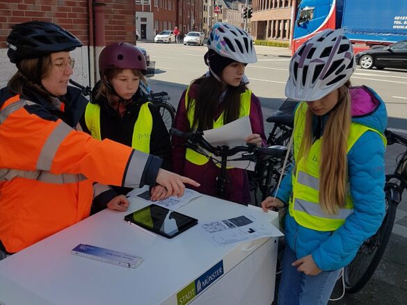 Besprechung der Fahrradplanerin mit den drei Schülerinnen an einer viel befahrenen Kreuzung.