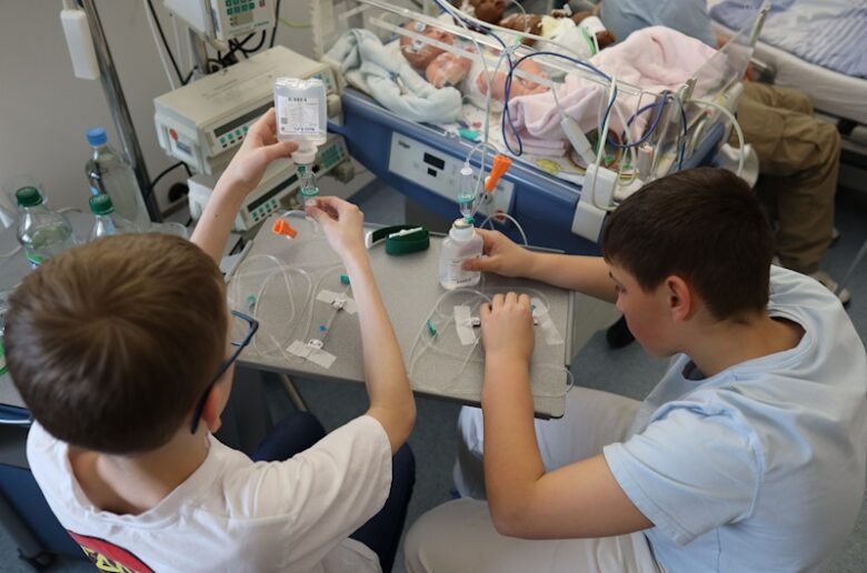 Zwei Jungen prüfen eine Infusionseinstellung auf der Kinderstation. Die Patienten sind 2 Puppen.