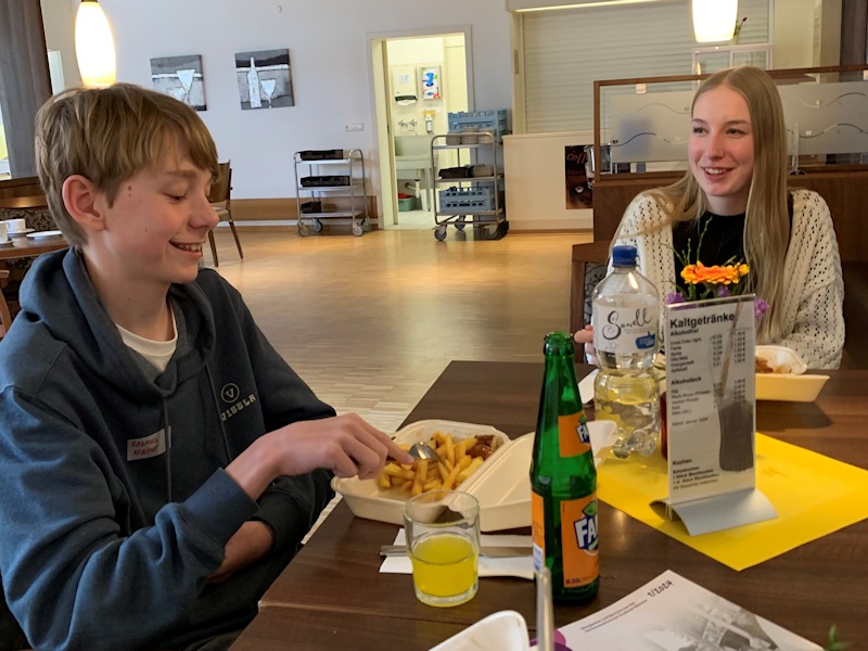 Der Tagespraktikant sitzt mit Pauline im Speisesaal und verzehrt sein Mittagessen