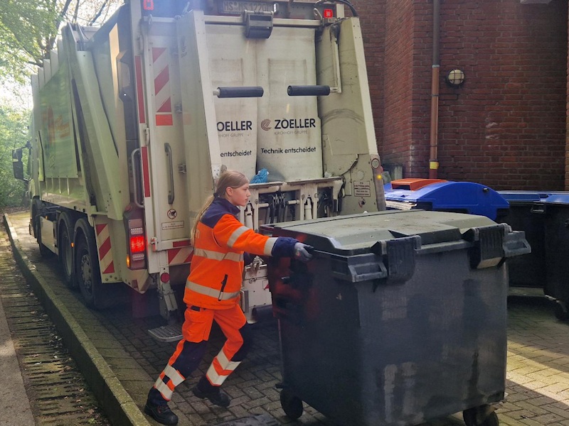 Eine Schlüerin schiebt eine restmülltonne zum LKW für die Leerung.