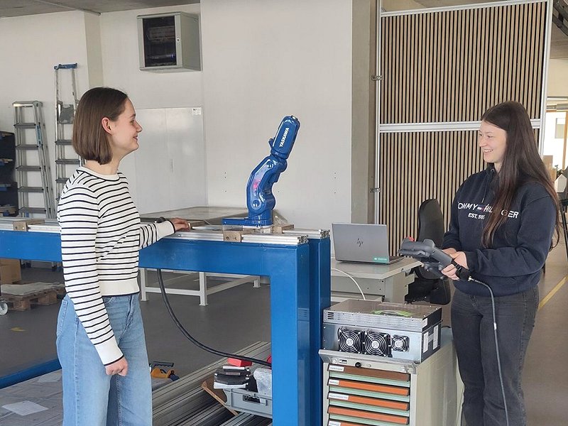 Die beiden teilnehmenden Schülerinnen Ella und Leonie stehen vor einer Maschine der Firma und betrachten die Technik.