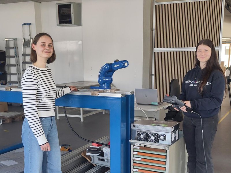 Die beiden teilnehmenden Schülerinnen Ella und Leonie stehen vor einer Maschine der Firma und lächeln in die Kamera.